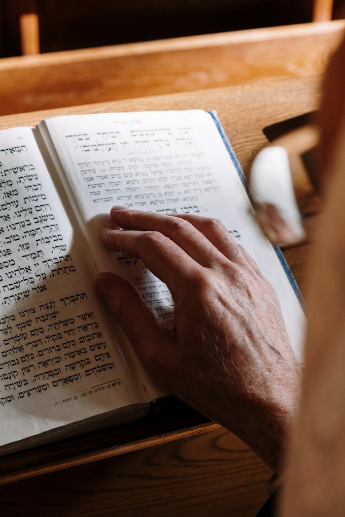 Close-up of an elderly hand on a Hebrew Torah text in a synagogue setting.